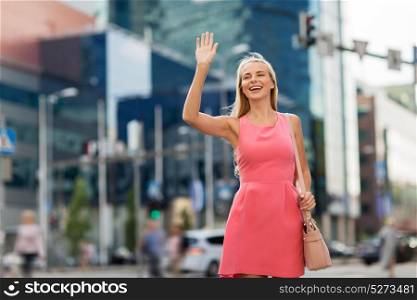gesture, lifestyle and people concept - happy young woman waving hand on city street. happy young woman waving hand on city street
