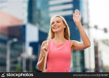 gesture, lifestyle and people concept - happy young woman waving hand on city street. happy young woman waving hand on city street