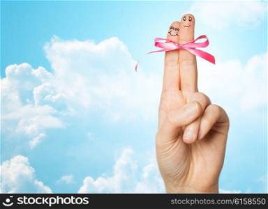 gesture, love, holidays and body parts concept - close up of hand with two fingers tied by pink bow knot over blue sky and clouds background