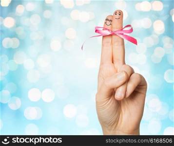 gesture, love, holidays and body parts concept - close up of hand with two fingers tied by pink bow knot over blue holidays lights background