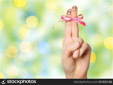 gesture, love, holidays and body parts concept - close up of hand with two fingers tied by pink bow knot over green summer holidays lights background