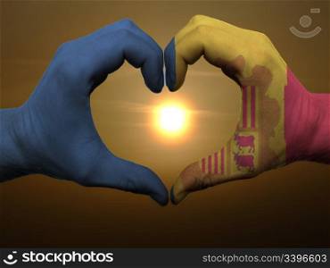 Gesture made by andora flag colored hands showing symbol of heart and love during sunrise