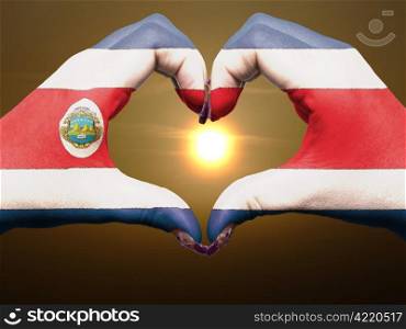 Gesture made by costa rica flag colored hands showing symbol of heart and love during sunrise