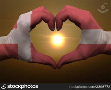 Gesture made by denmark flag colored hands showing symbol of heart and love during sunrise