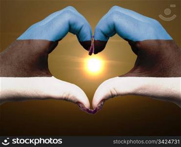 Gesture made by estonia flag colored hands showing symbol of heart and love during sunrise