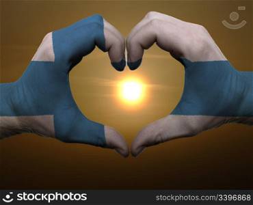 Gesture made by finland flag colored hands showing symbol of heart and love during sunrise