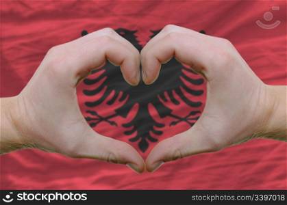 Gesture made by hands showing symbol of heart and love over Albanian flag