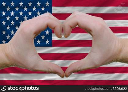 Gesture made by hands showing symbol of heart and love over american flag