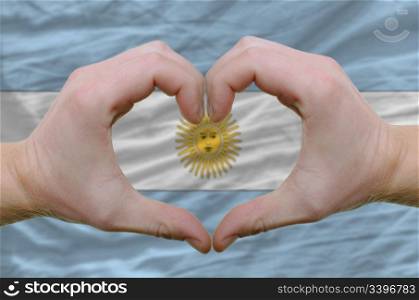 Gesture made by hands showing symbol of heart and love over argentinian flag