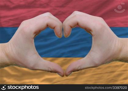 Gesture made by hands showing symbol of heart and love over armenian flag