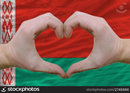 Gesture made by hands showing symbol of heart and love over belarus flag