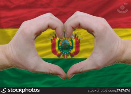 Gesture made by hands showing symbol of heart and love over bolivia flag