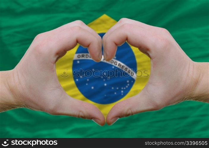 Gesture made by hands showing symbol of heart and love over brazil flag