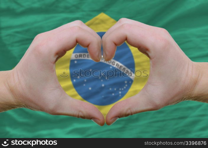 Gesture made by hands showing symbol of heart and love over brazilian flag