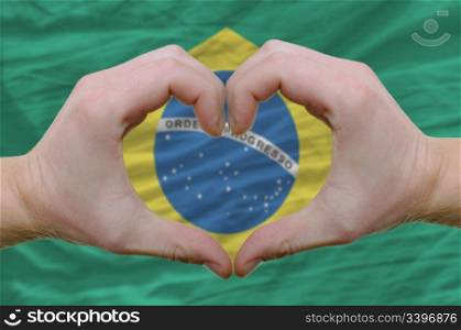 Gesture made by hands showing symbol of heart and love over brazilian flag