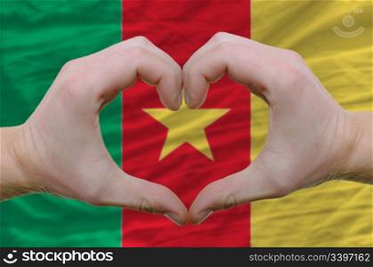 Gesture made by hands showing symbol of heart and love over cameroon flag