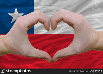 Gesture made by hands showing symbol of heart and love over chile flag