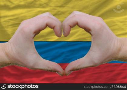 Gesture made by hands showing symbol of heart and love over columbia flag
