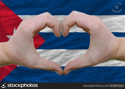 Gesture made by hands showing symbol of heart and love over cuba flag