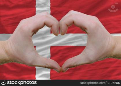 Gesture made by hands showing symbol of heart and love over denmark flag