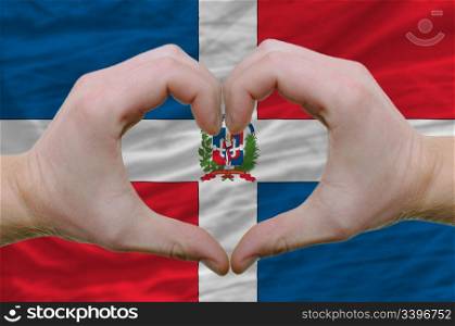 Gesture made by hands showing symbol of heart and love over dominican flag