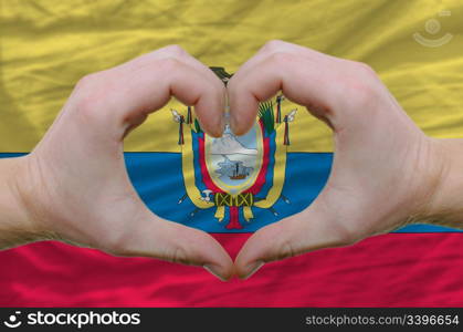 Gesture made by hands showing symbol of heart and love over ecuador flag