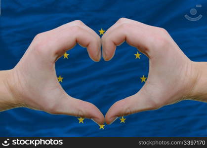 Gesture made by hands showing symbol of heart and love over european union flag