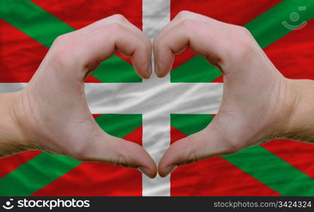 Gesture made by hands showing symbol of heart and love over flag of basque