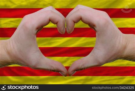 Gesture made by hands showing symbol of heart and love over flag of catalonia