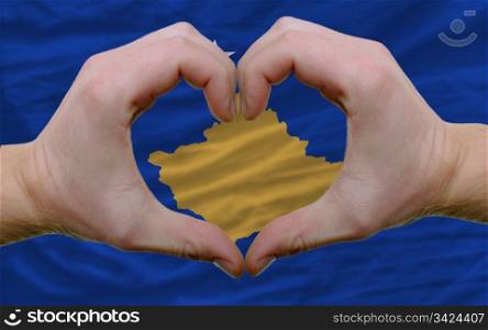 Gesture made by hands showing symbol of heart and love over flag of kosovo