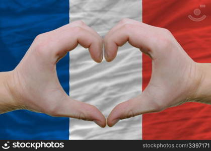 Gesture made by hands showing symbol of heart and love over france flag