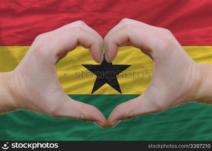 Gesture made by hands showing symbol of heart and love over ghana flag