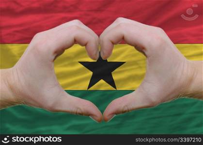 Gesture made by hands showing symbol of heart and love over ghana flag