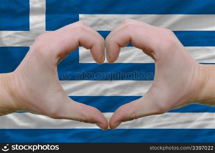 Gesture made by hands showing symbol of heart and love over greece flag