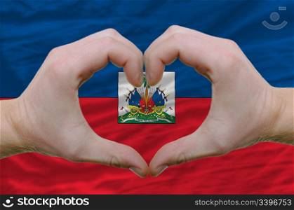 Gesture made by hands showing symbol of heart and love over haiti flag