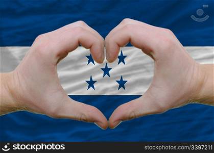 Gesture made by hands showing symbol of heart and love over honduras flag
