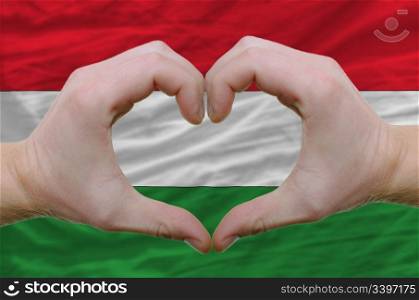 Gesture made by hands showing symbol of heart and love over hungary flag