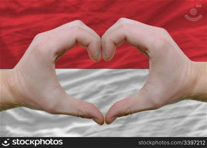 Gesture made by hands showing symbol of heart and love over indonesia flag