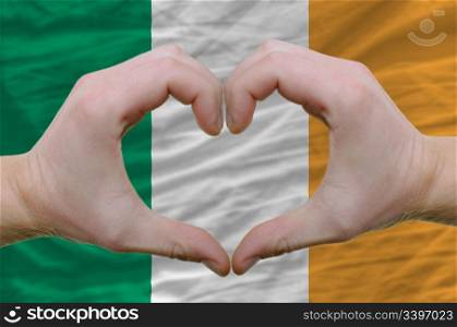 Gesture made by hands showing symbol of heart and love over ireland flag