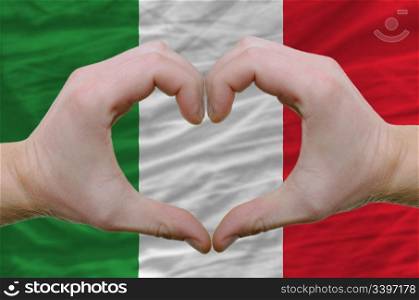 Gesture made by hands showing symbol of heart and love over italy flag