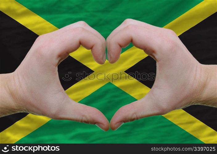 Gesture made by hands showing symbol of heart and love over jamaica flag