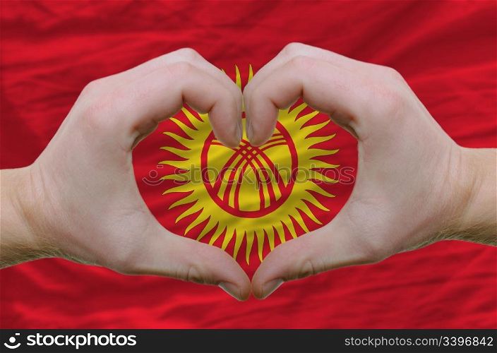 Gesture made by hands showing symbol of heart and love over kyrghyzstan flag