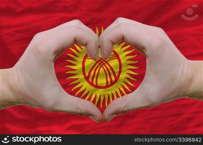 Gesture made by hands showing symbol of heart and love over kyrghyzstan flag