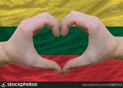 Gesture made by hands showing symbol of heart and love over lithuania flag