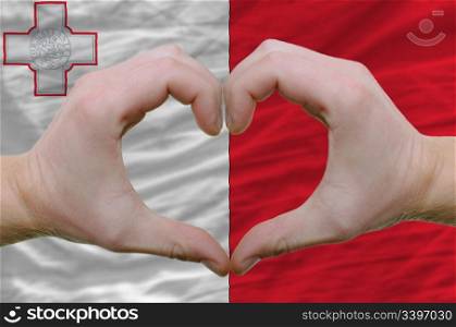 Gesture made by hands showing symbol of heart and love over malta flag
