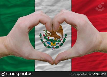 Gesture made by hands showing symbol of heart and love over mexico flag