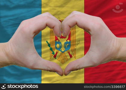 Gesture made by hands showing symbol of heart and love over moldova flag