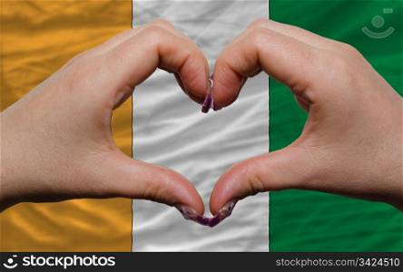 Gesture made by hands showing symbol of heart and love over national cote&rsquo;d ivore flag