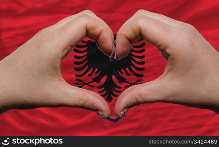 Gesture made by hands showing symbol of heart and love over national albania flag