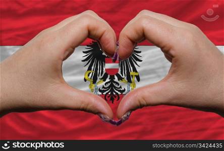 Gesture made by hands showing symbol of heart and love over national austria flag